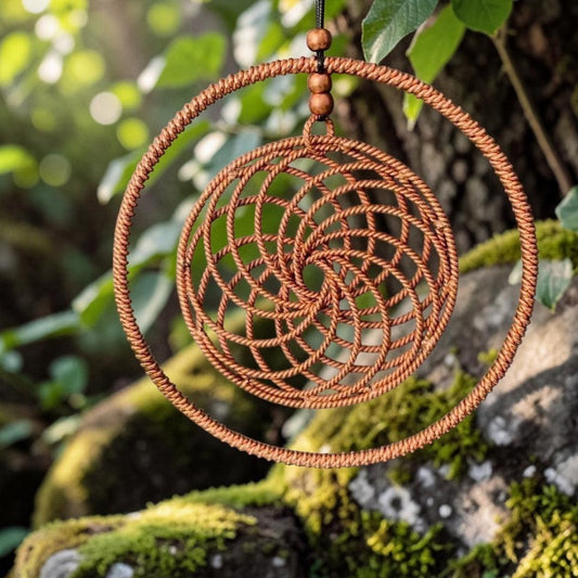 Handmade copper vortex coil pendant with a woven spiral mesh, 144MHz Sacred Cubit, on a mossy rock