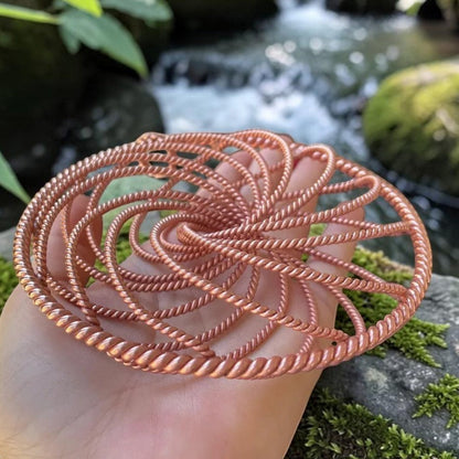 Copper spiral vortex disc held in a hand for scale, worn as a pendant or kept as a desk piece