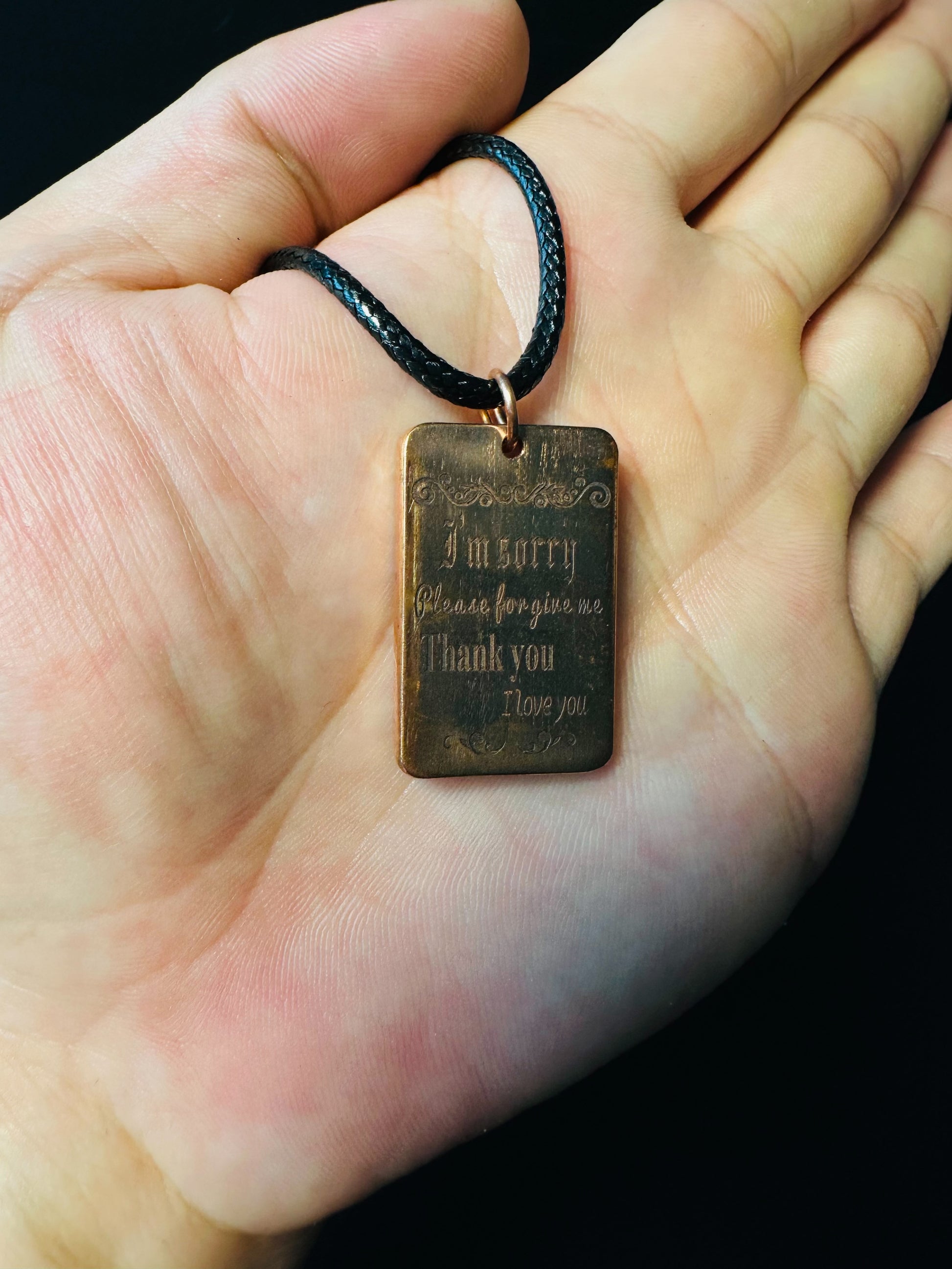 Ho'oponopono copper pendant held in a palm, showing its compact size and engraved prayer