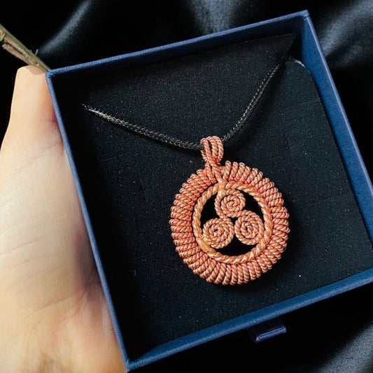 Round copper sacred geometry pendant in a black gift box, showing the fine triple spiral detail