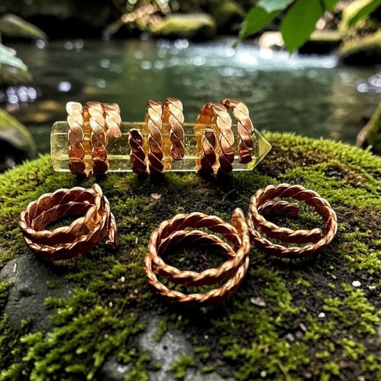 Several spiral copper rings arranged on mossy stone, showing the open hand-coiled design