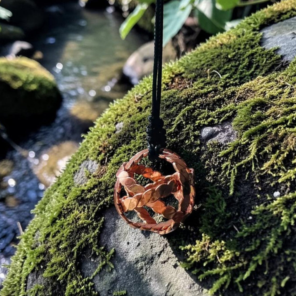 Twisted four-strand copper tensor bracelet resting on a stream-side rock, pure red copper coil bangle