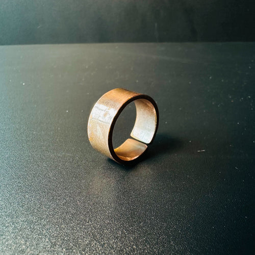 Handmade wide copper ring with a smooth flat band and warm patina, standing on a dark surface
