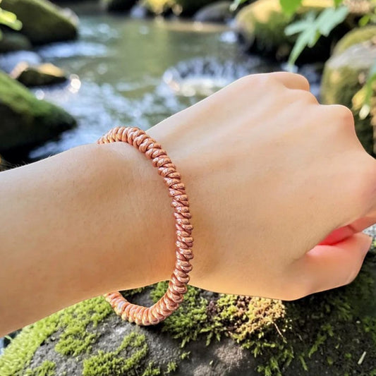 Woven copper tensor bracelet worn on a wrist outdoors by a stream, a handmade open coil bangle